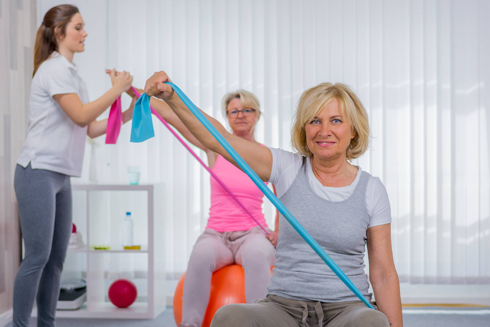senioren machen übungen mit dem theraband auf dem pezziball